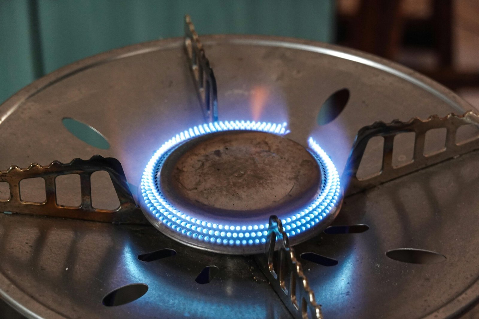 A detailed view of a lit gas stove burner with visible blue flames and metal support.