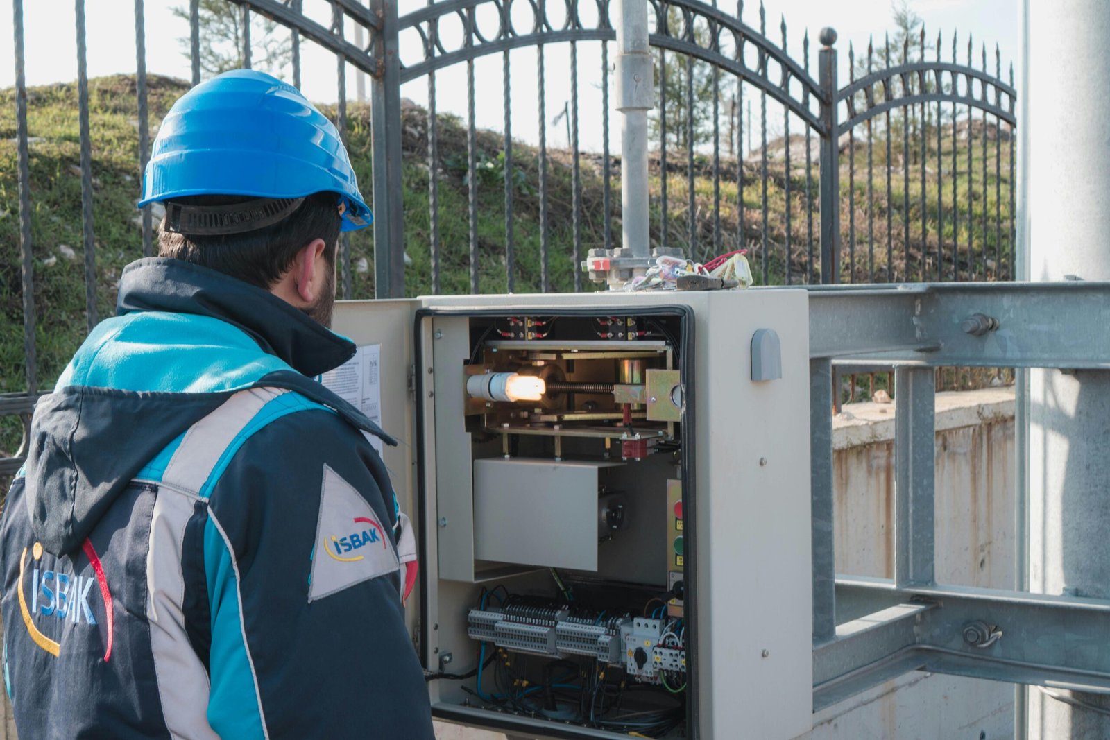 A professional electrician wearing a hard hat inspects an outdoor fuse box ensuring safety.